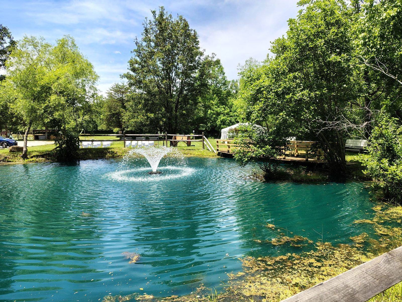 The pond with fountain, split-rail fence and tent field at Riverside Farm Venue