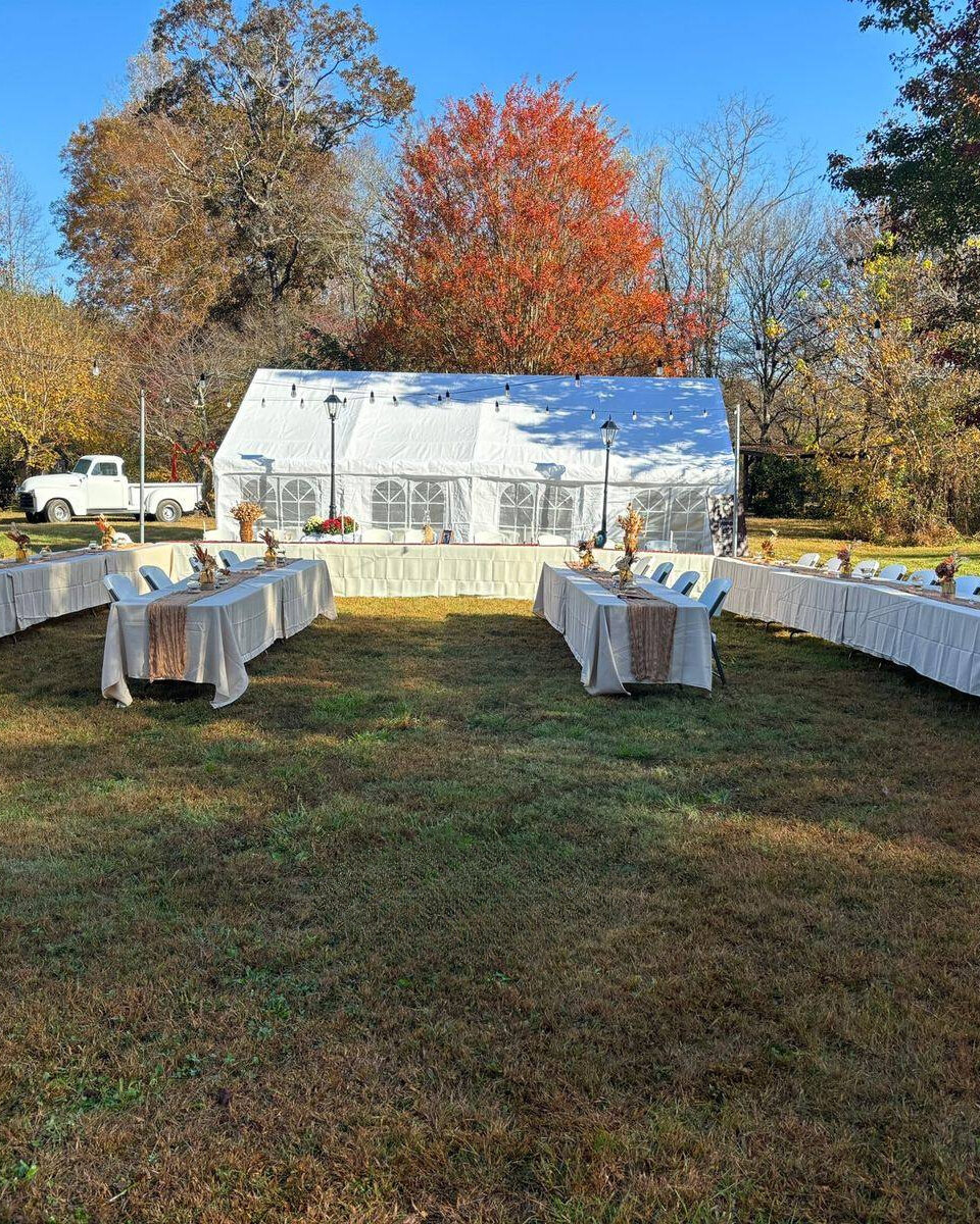 Long tables and chairs set up in the open field in front of the white tent at Riverside Farm Venue