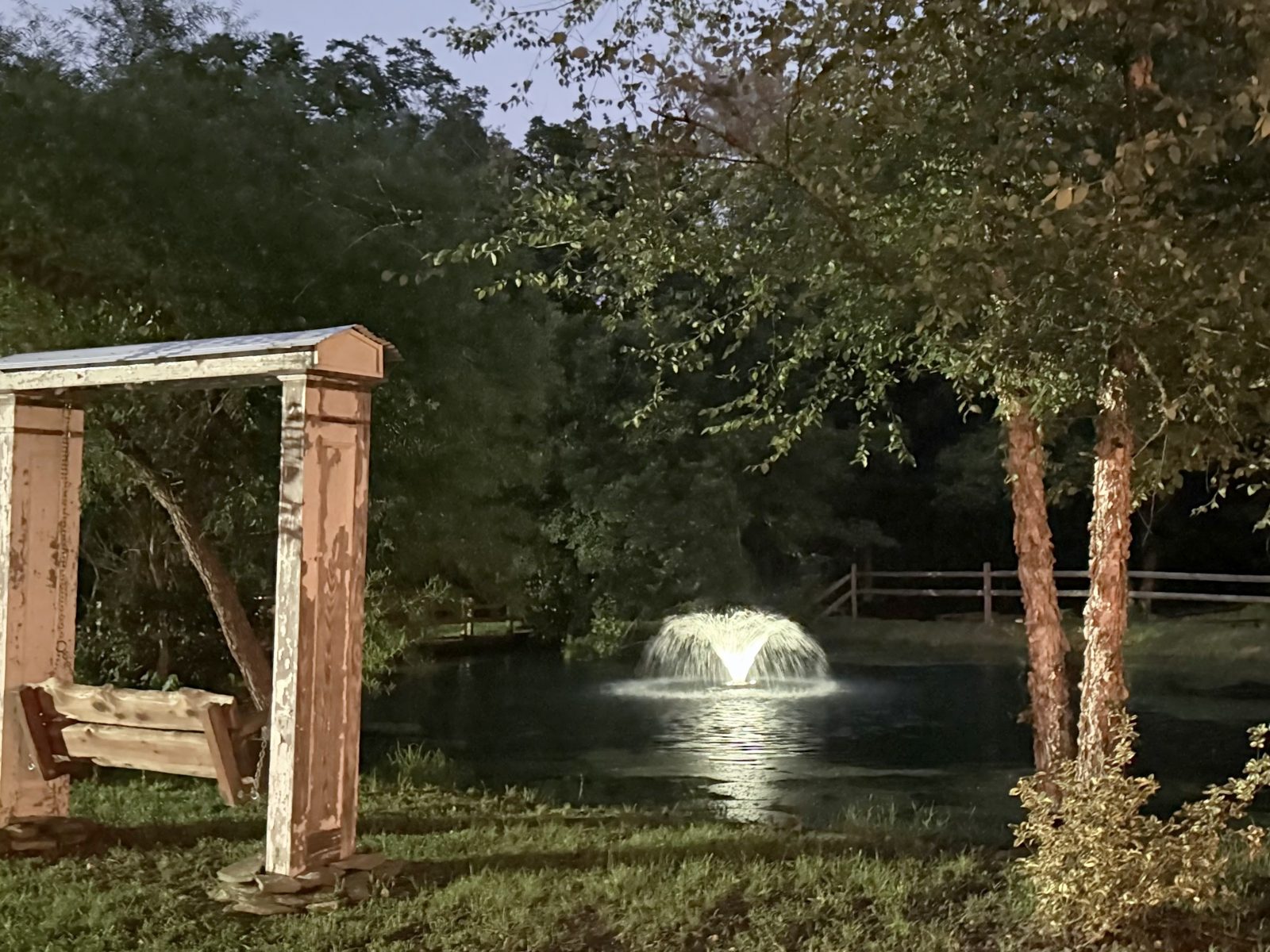 A porch swing frame by the pond with the fountain at dusk at Riverside Farm Venue