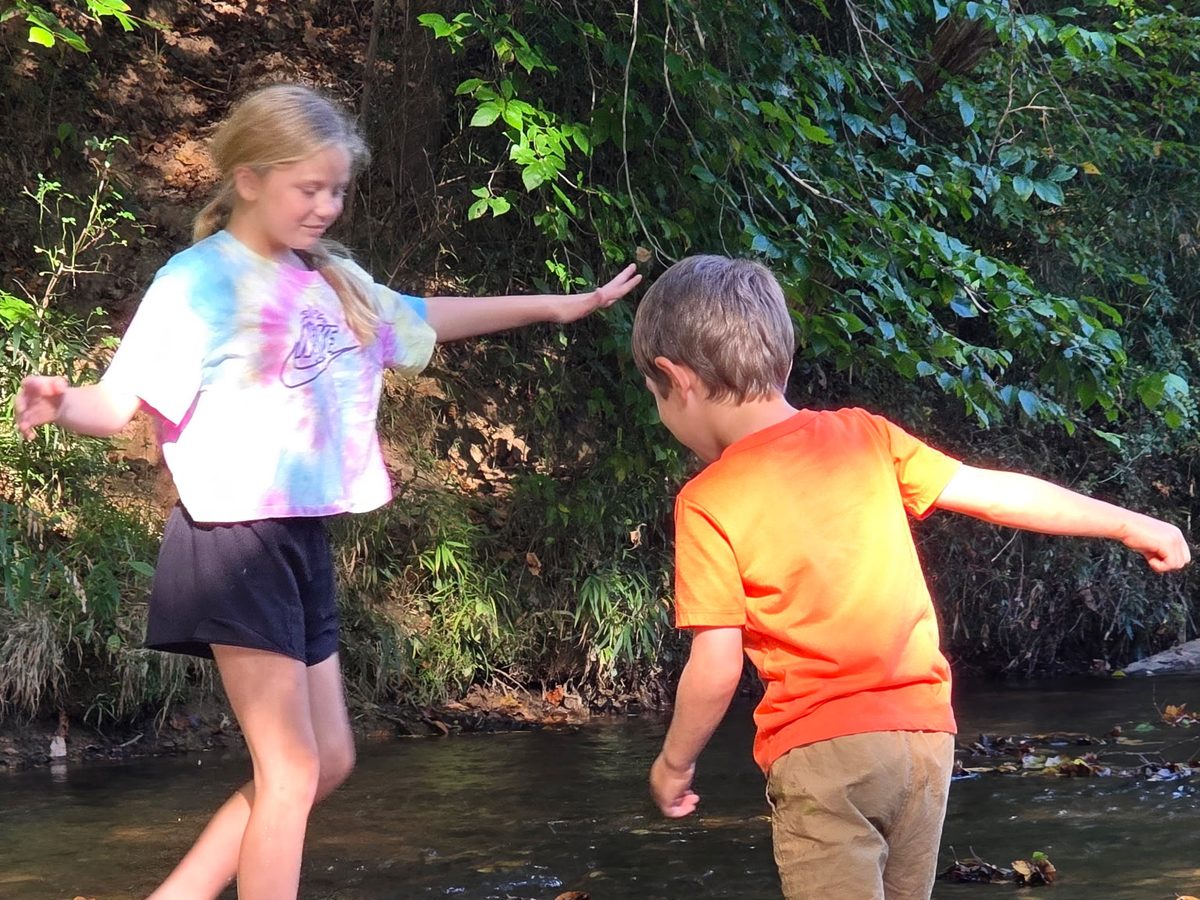 A girl and boy wading across the river together at Riverside Farm Venue