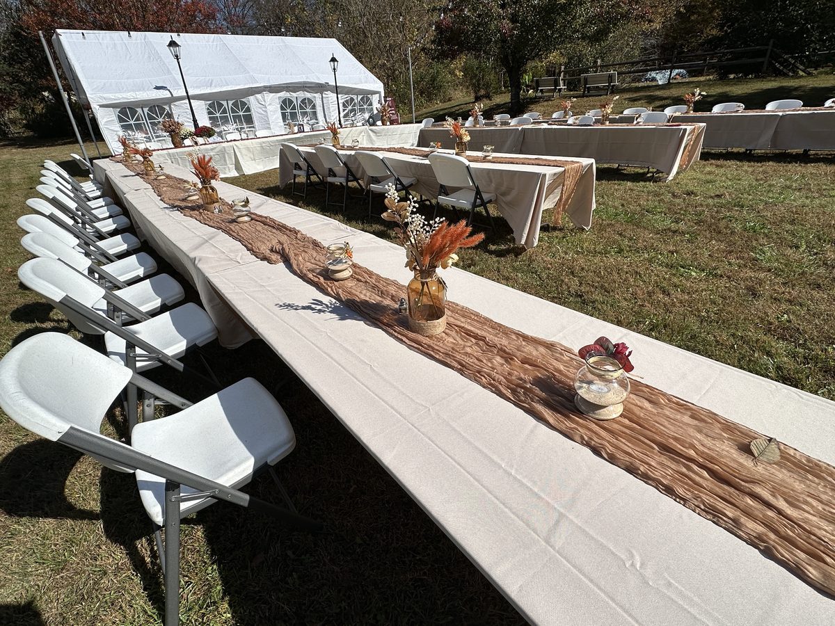 Long tables and white chairs set up on the field in front of the white tent at Riverside Farm Venue