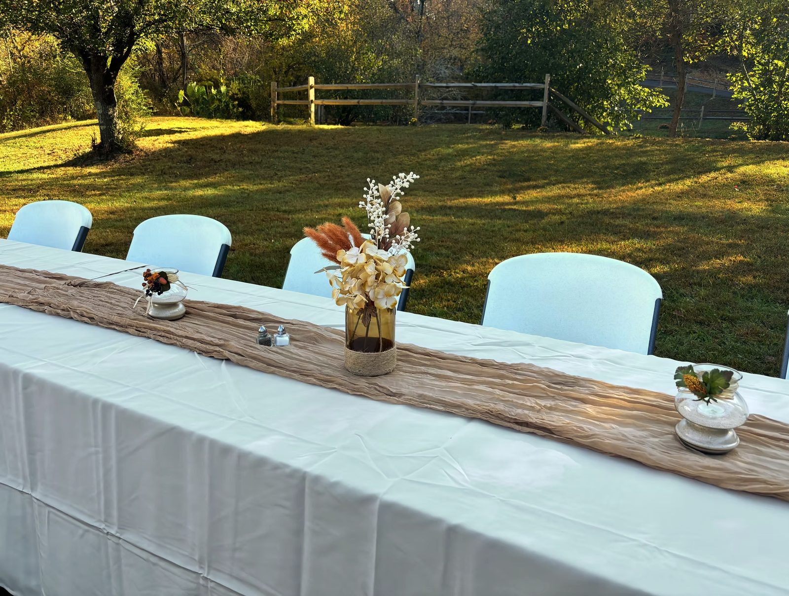 Long table with white cloth, burlap runner and dried-floral centerpieces on the lawn at Riverside Farm Venue