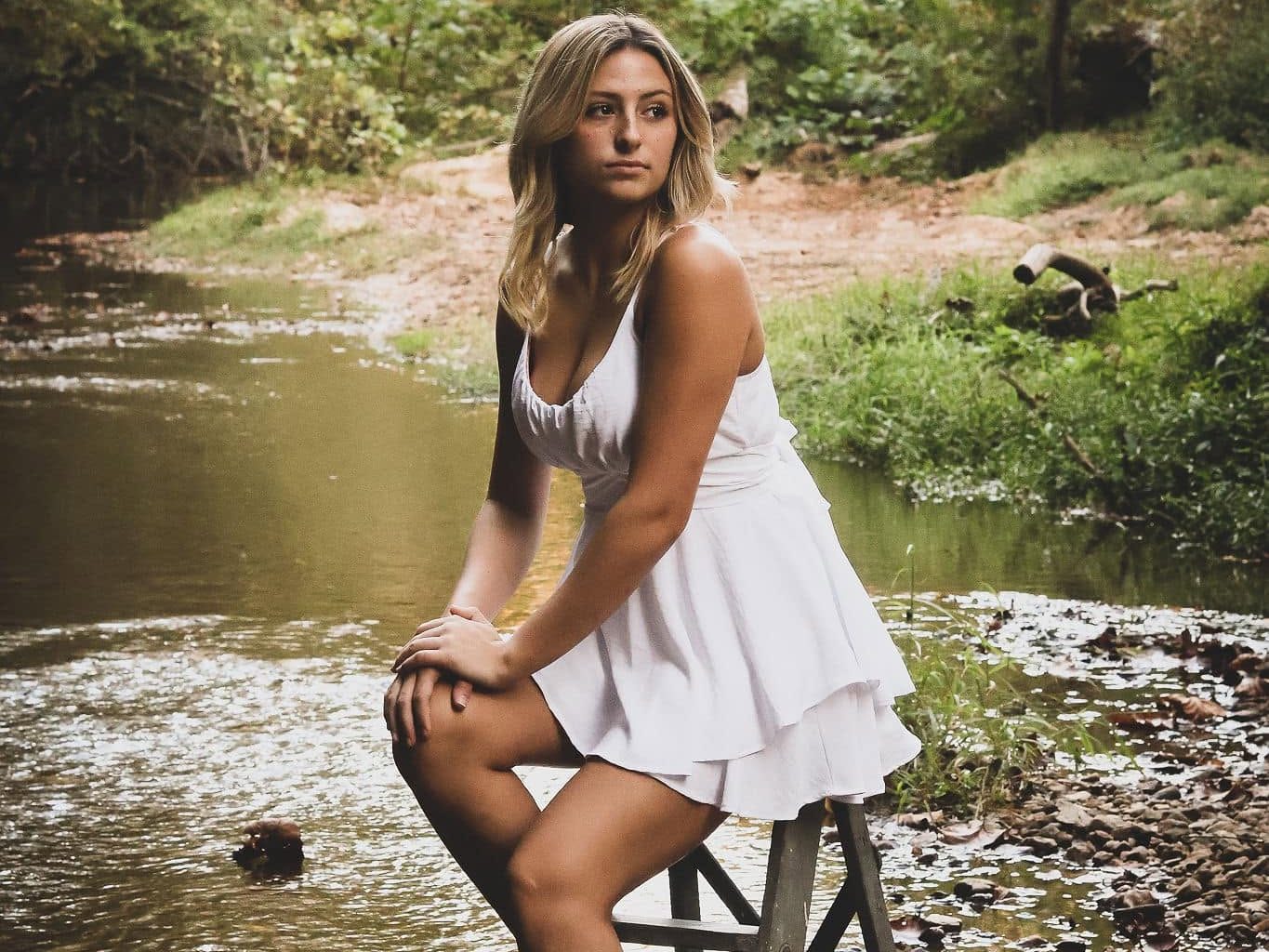 Portrait session with a young woman in a white dress seated on a wooden ladder in the river at Riverside Farm Venue (photo: Yahaira Vazquez)