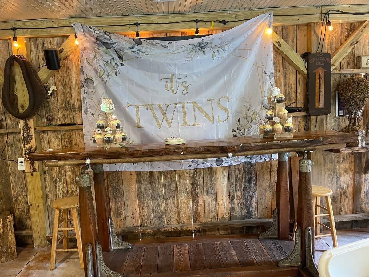 Twins baby shower set up at the rustic barn bar with string lights, cupcakes and an It’s Twins banner at Riverside Farm Venue