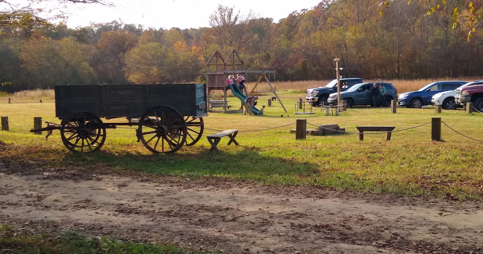 The wooden playground and slide beside the field, with an antique wagon in front and free on-site parking in the field, at Riverside Farm Venue