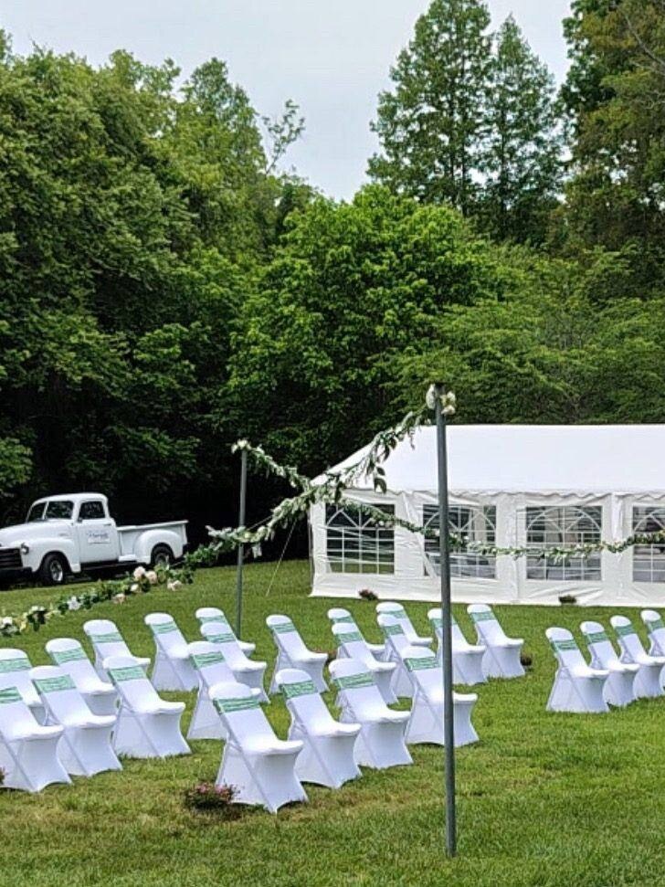 White chairs set up on the field in front of the white tent, with a white pickup truck parked beside it at Riverside Farm Venue