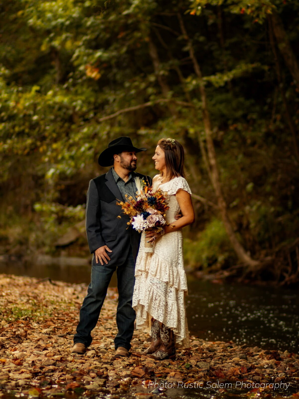 Bride and groom standing by the river among fall leaves at Riverside Farm Venue