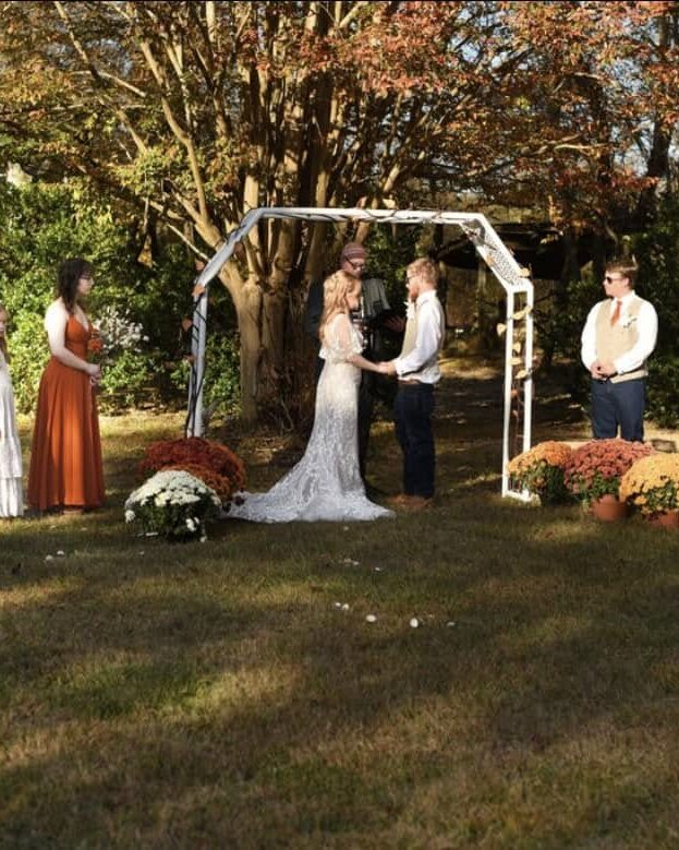 Fall ceremony on the lawn with the couple and wedding party under the white arch at Riverside Farm Venue