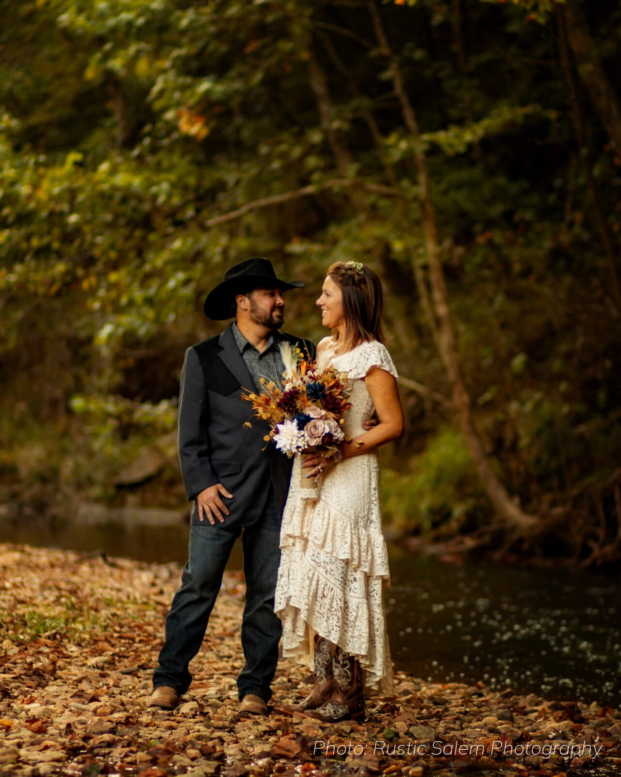 Bride and groom standing by the river among fall leaves at Riverside Farm Venue